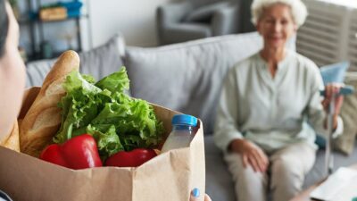 Assisted living caregiver delivers groceries to woman at home.