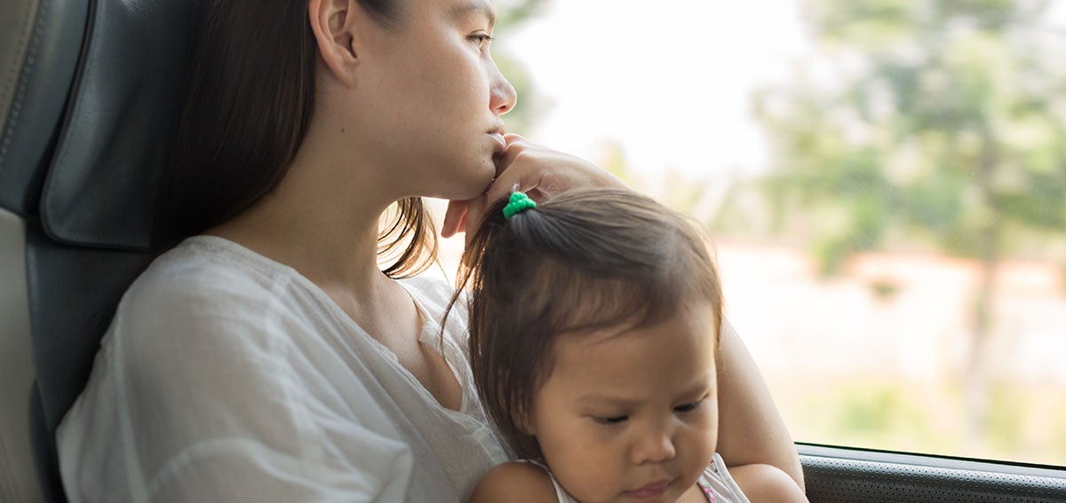 Mother holds baby and looks off into the distance, while sitting in car